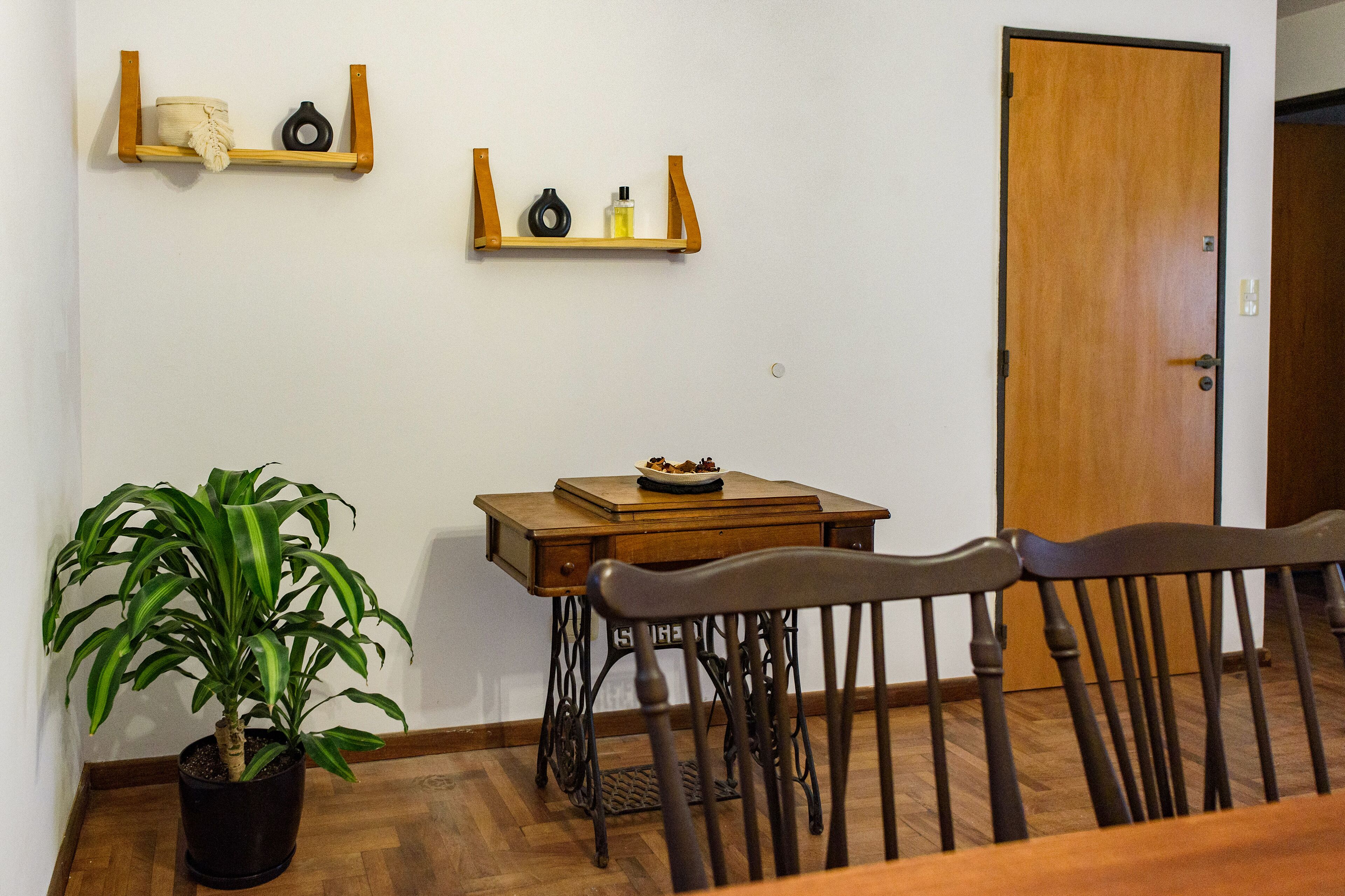 A dining area with a wooden table, chairs, a potted plant, and a sewing machine.
