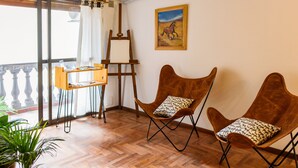 A room with a wooden floor, two brown chairs with patterned cushions, a wooden easel, and a painting of a horse on the wall. - Cosy Local Artist's Flat, Central Location, Fully Equipped (Córdoba)
