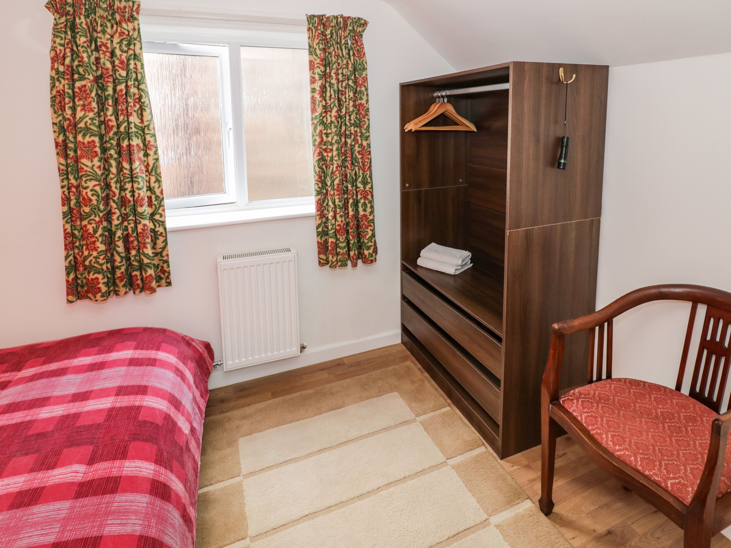 A room with a bed, a wooden wardrobe, a chair, and a window with curtains.