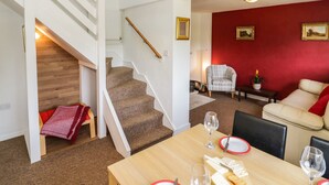 A dining area with a wooden table set for four, a staircase, and a red wall with framed pictures. - 3 Oaks Lodge (Shrewsbury)