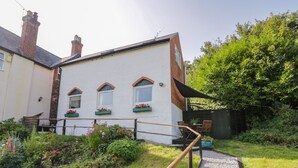 A white building with three windows, a wooden deck, and a gravel path leading to a seating area. - 3 Oaks Lodge (Shrewsbury)