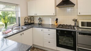 A modern kitchen with white cabinets, granite countertops, a black range hood, a built-in oven, and a microwave. - 3 Oaks Lodge (Shrewsbury)