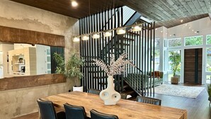 A modern dining area with a wooden table and chairs, a decorative vase, and a staircase with a railing. - Brand new! Modern Lake Whatcom View home (Bellingham)