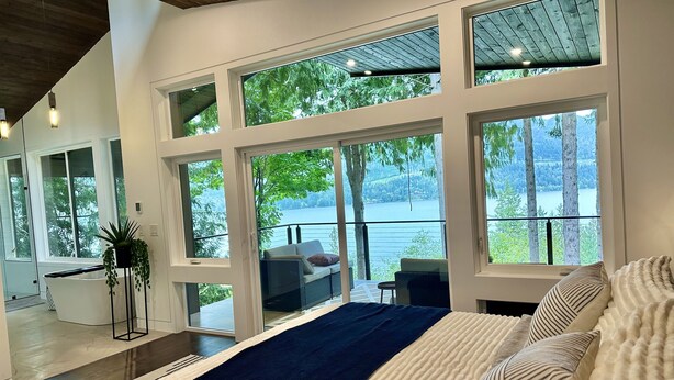 A modern bedroom with large windows, a bed, and a view of a lake. - Brand new! Modern Lake Whatcom View home (Bellingham)