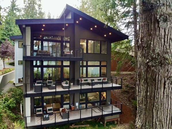 Une maison moderne à plusieurs étages, dotée de grandes fenêtres, de balcons et d’espaces de détente en plein air.