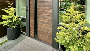 A modern building entrance with large windows, a wooden facade, and two potted plants. - Brand new! Modern Lake Whatcom View home (Bellingham)