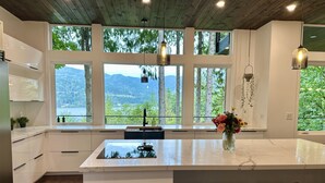 A modern kitchen with large windows, a central island, and bar stools. - Brand new! Modern Lake Whatcom View home (Bellingham)