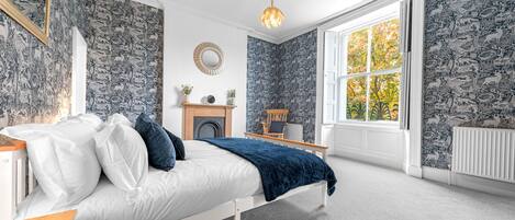 Une chambre à coucher comprenant un lit, une commode, un miroir, une cheminée et une fenêtre donnant sur la forêt.