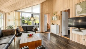 Un soggiorno moderno con soffitto in legno, un divano in pelle nera, un tavolino in legno e una grande TV a schermo piatto.