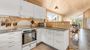 Una cucina moderna con mobili bianchi, forno integrato e microonde. Si intravede un'area pranzo con tavolo e sedie attraverso ampie finestre.