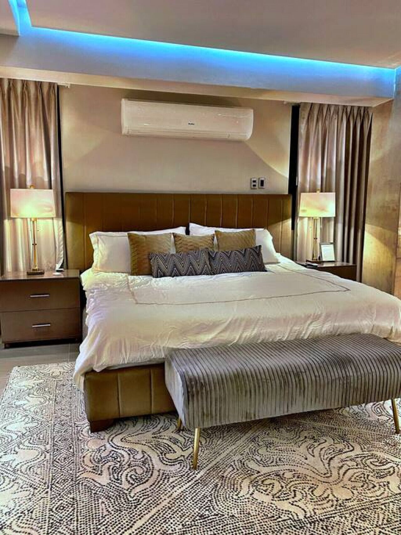 Une chambre d’hôtel moderne avec un grand lit, une table de chevet, une petite table d’appoint, un tapis à motifs et un climatiseur au plafond.