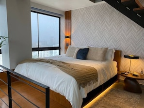 Quarto moderno com uma cama grande, vista da cidade através de uma janela ampla e parede com padrão losango.