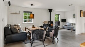 Ein modernes Wohnzimmer mit Kamin, einer Couch, einem Esstisch und Korbstühlen.