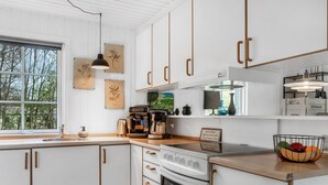 Eine moderne Küche mit weißen Schränken, Holzgriffen, einer Kaffeemaschine und einer Obstschale auf der Arbeitsplatte.