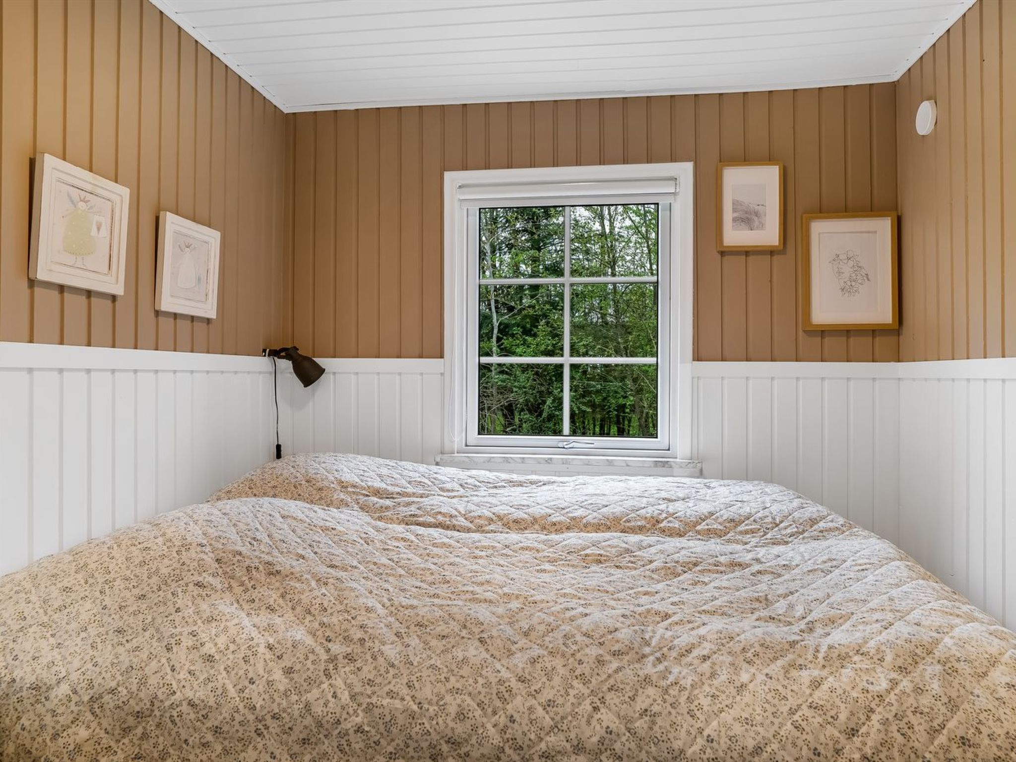 Ein Schlafzimmer mit einem großen Bett, einem Fenster mit Blick auf Bäume und an der Wand hängenden Bildern.