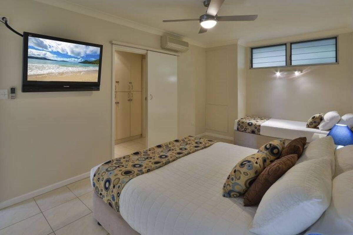 A bedroom with a bed, a ceiling fan, a TV, and a window with blinds.