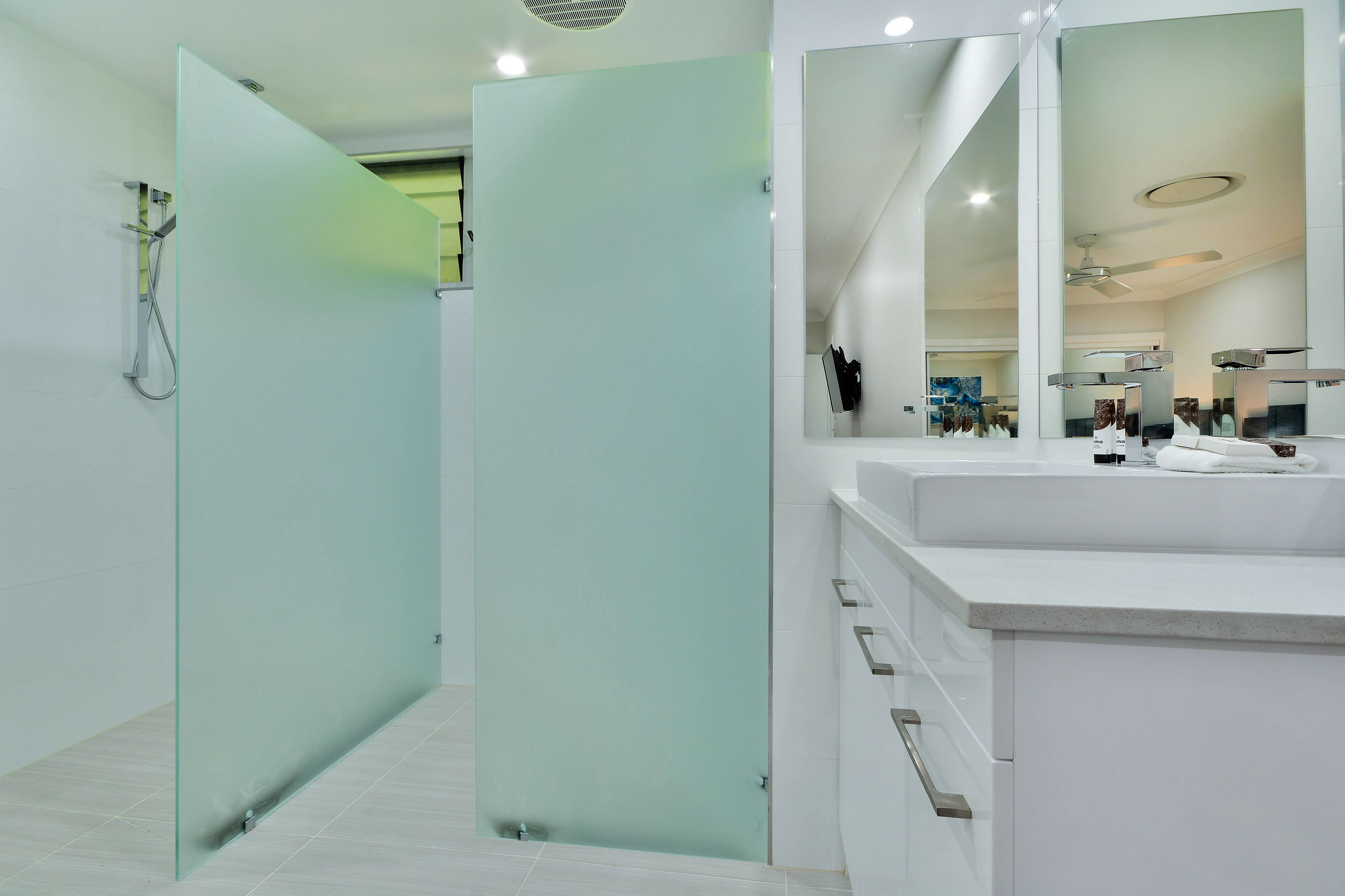 A modern bathroom with a glass partition, a large mirror, and a white sink.