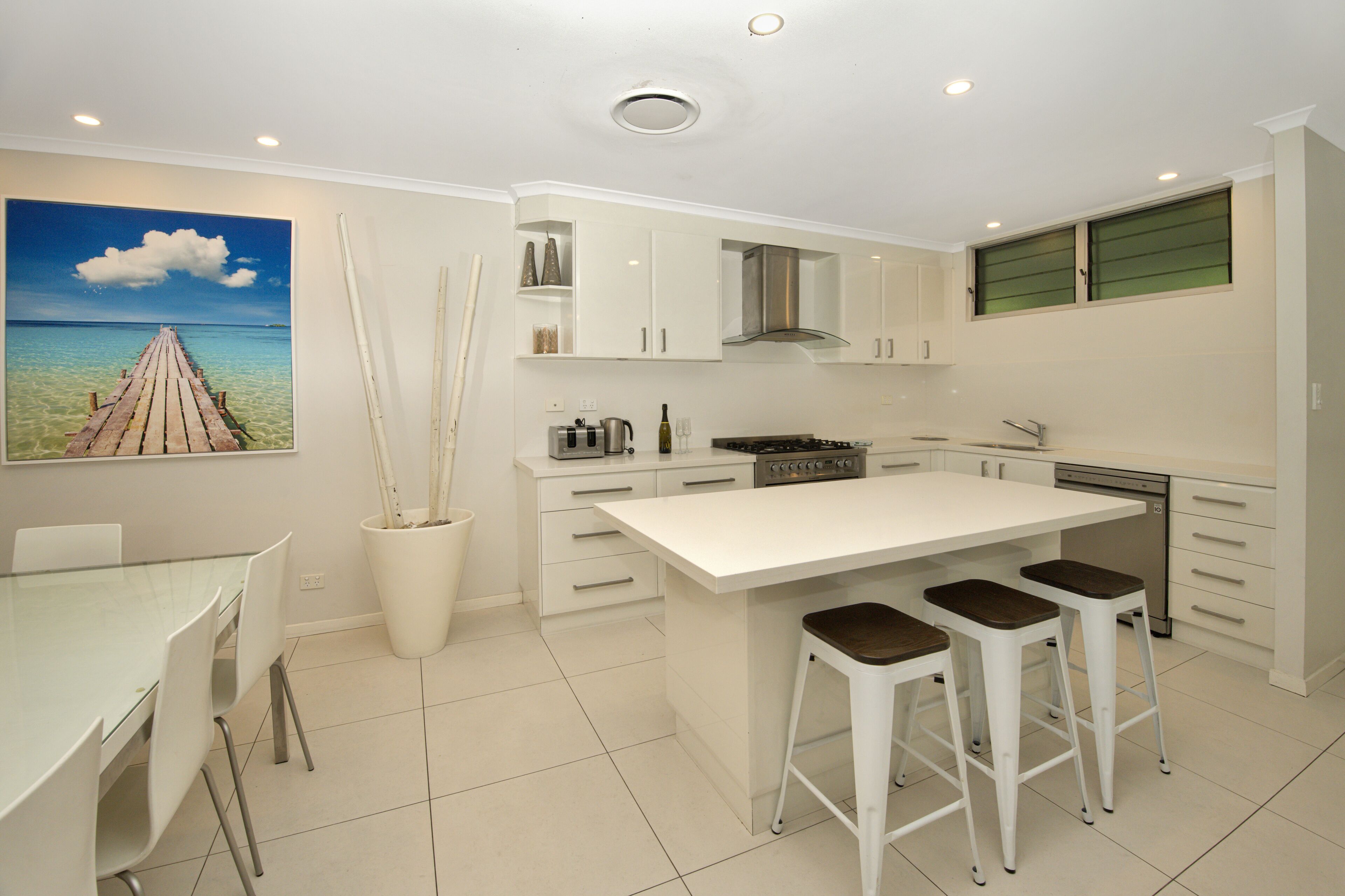 A modern kitchen with a central island, white cabinetry, and a dining area with a glass table and chairs.