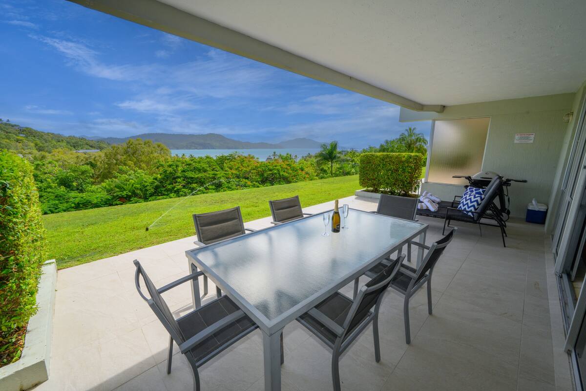 A patio with a table and chairs, a bottle of wine, and a view of the landscape.