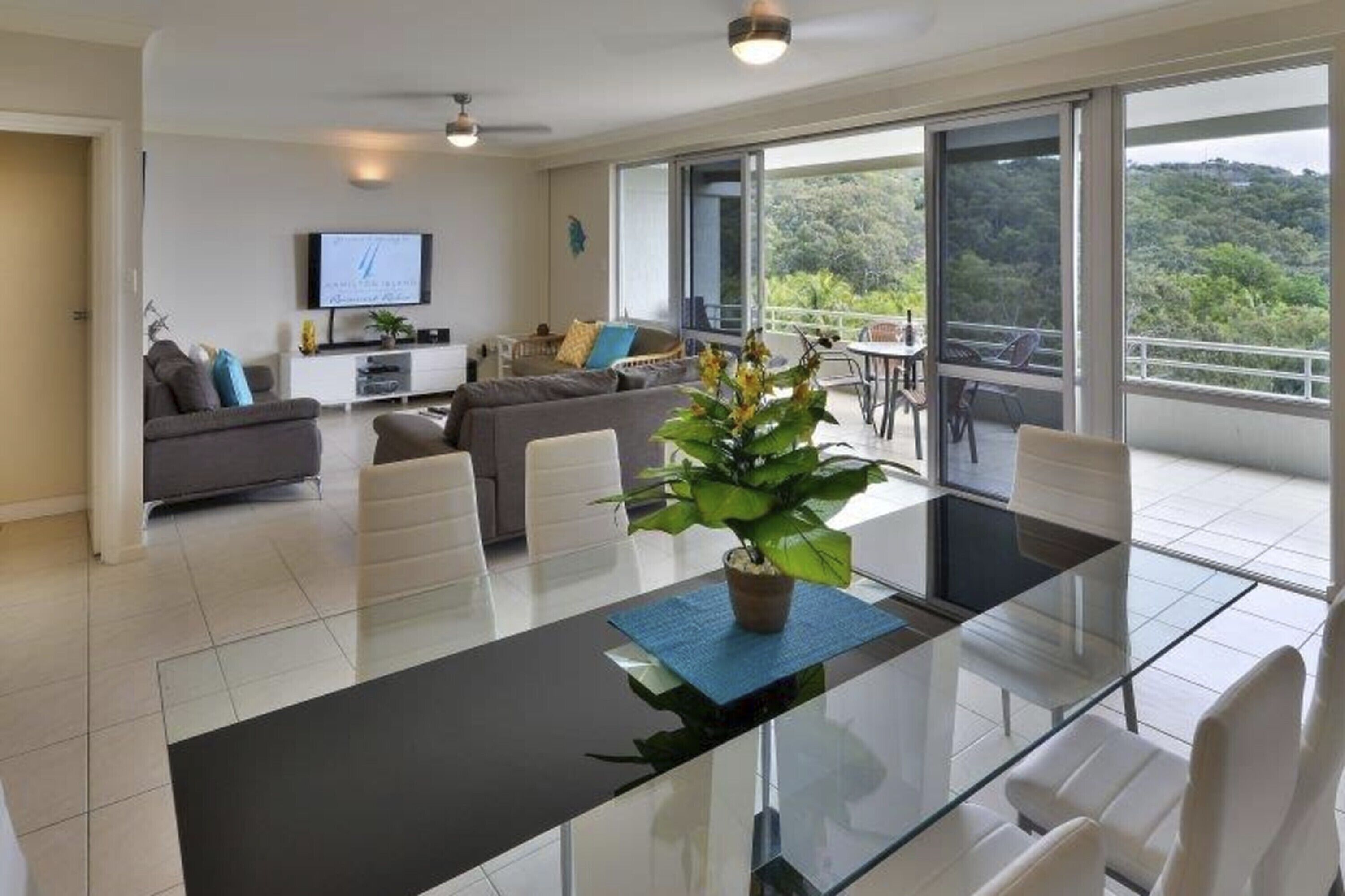 Un salon moderne avec une table à manger en verre, des canapés et une grande fenêtre donnant sur un paysage verdoyant.