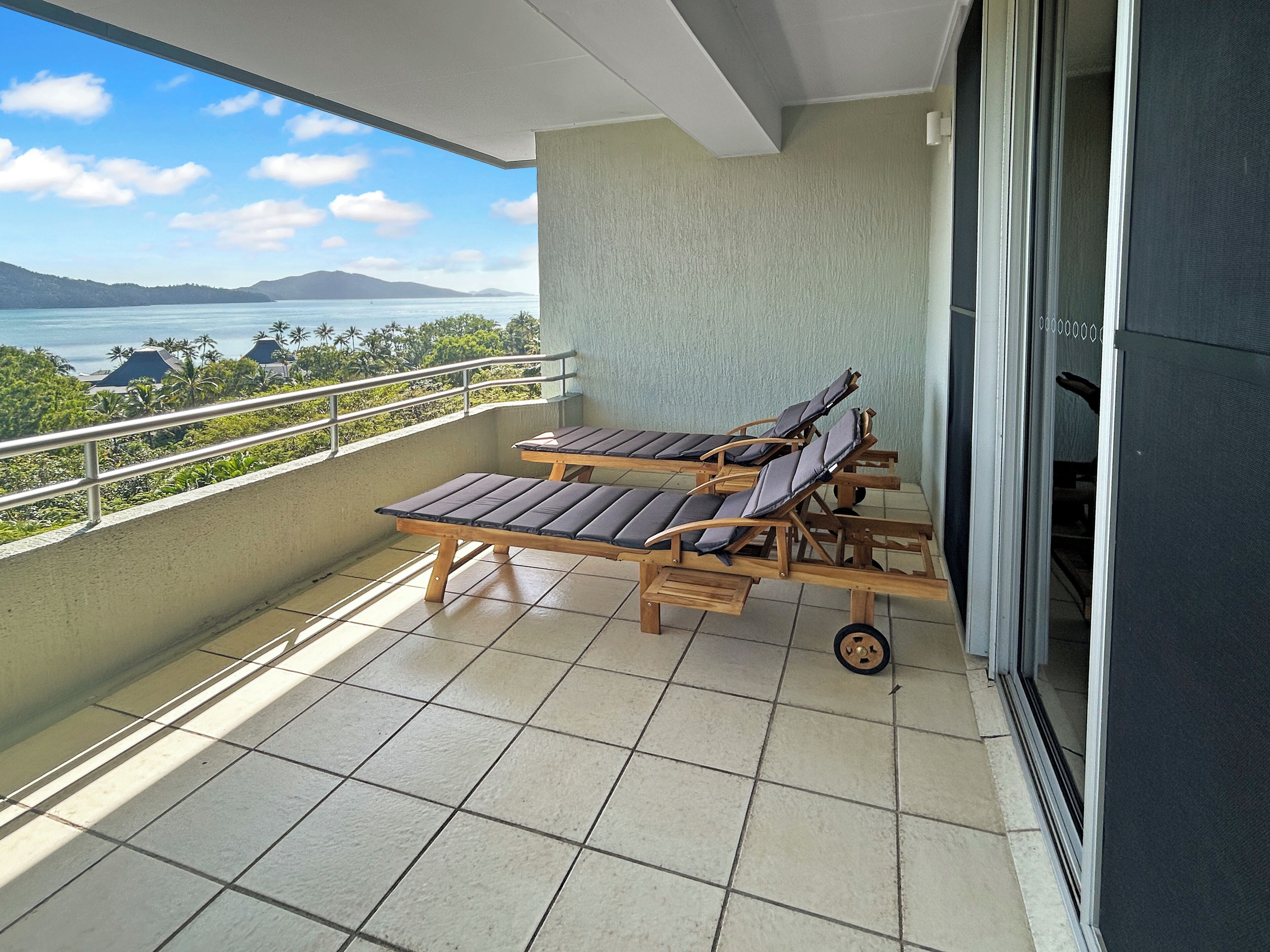 A balcony with two wooden lounge chairs and a view of the sea.