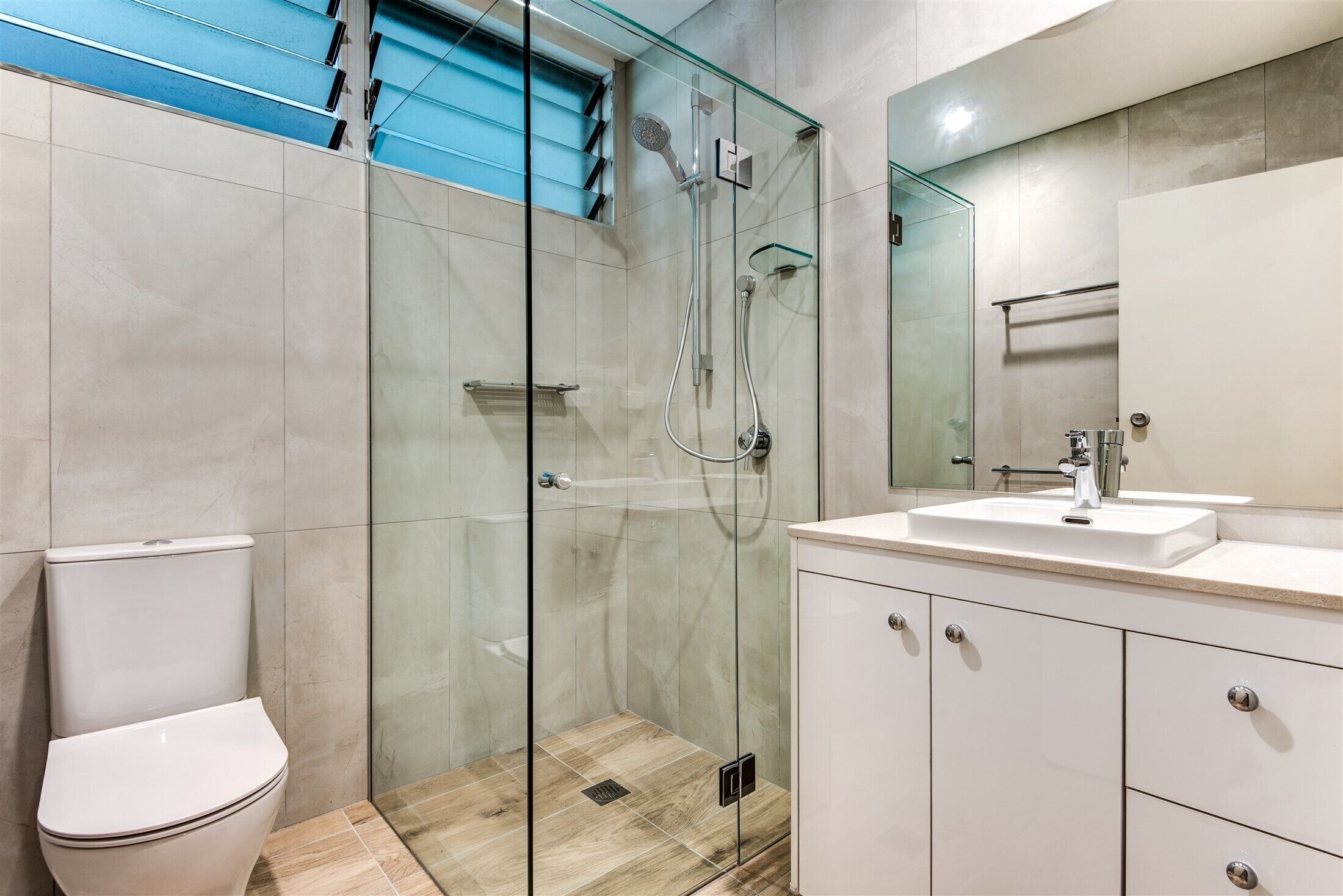 A modern bathroom with a glass-enclosed shower, a white toilet, and a vanity with a mirror.