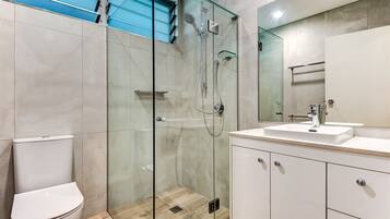 Un bagno moderno con doccia vetrata, un water bianco e un mobile lavabo con specchio.