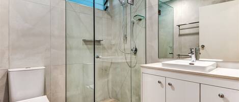 A modern bathroom with a glass-enclosed shower, a white toilet, and a vanity with a mirror.