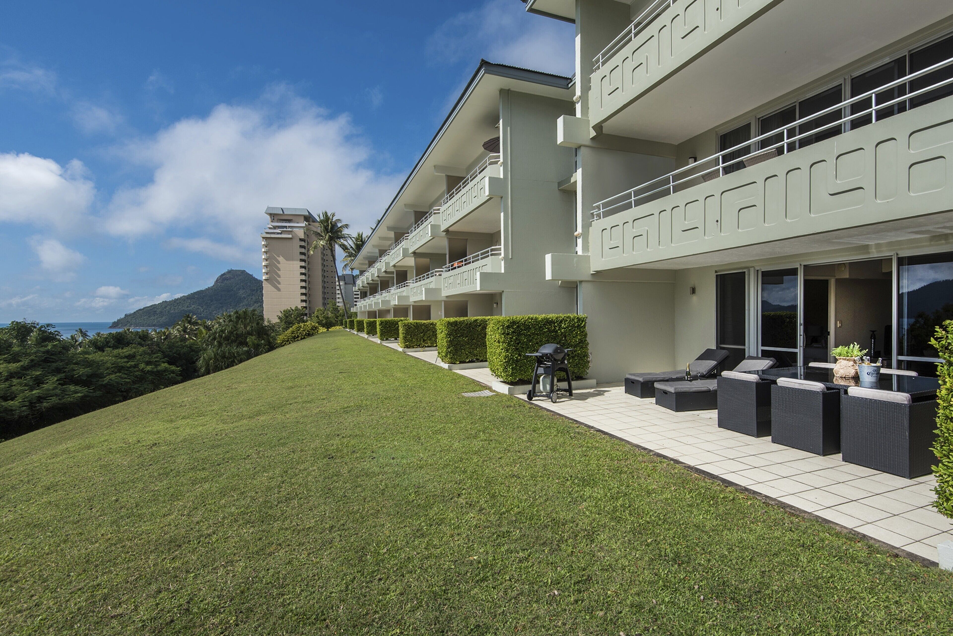 A modern hotel with a flat roof, multiple balconies, and a well-maintained lawn.