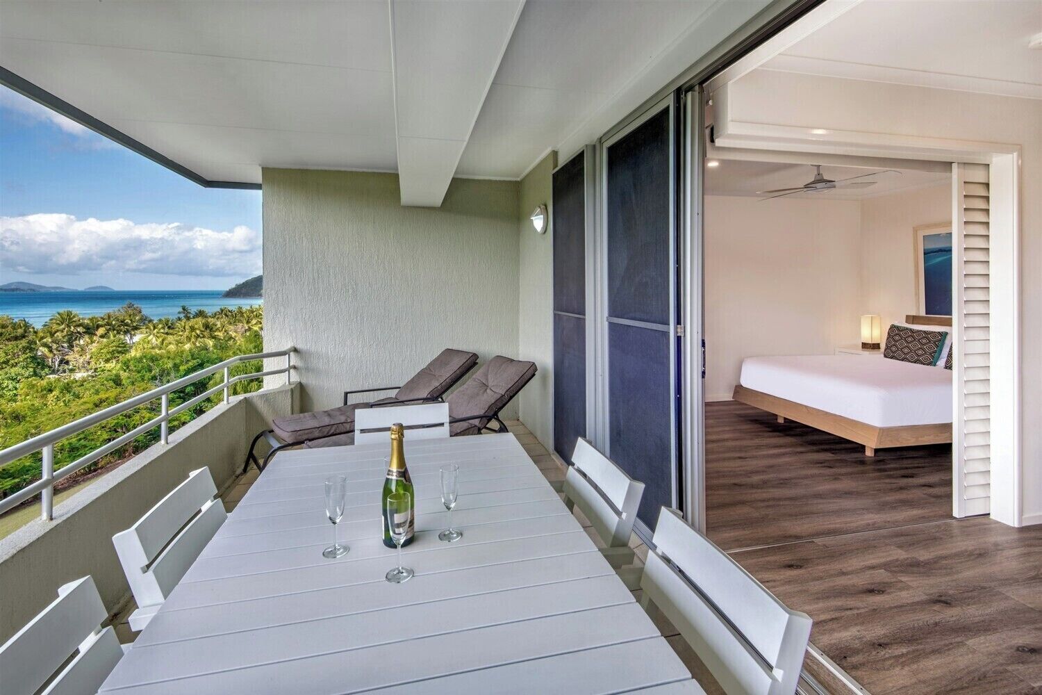 A balcony with a table set for two, a bottle of champagne, and two lounge chairs.