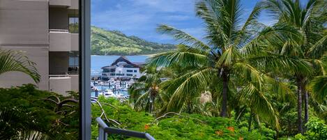 A balcony with a view of a marina, palm trees, and a hilly landscape.