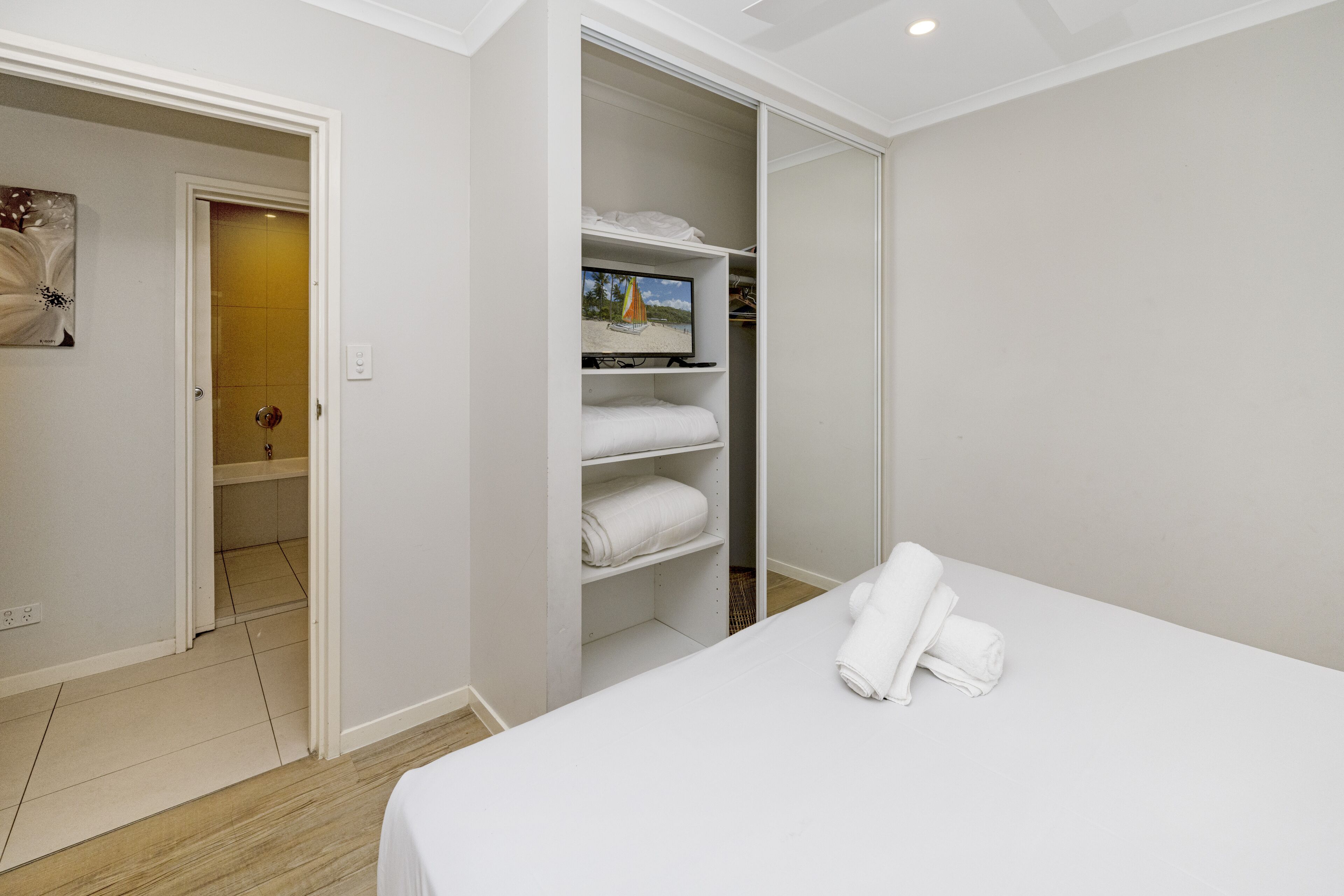 A hotel room with a bed, a closet with shelves, and a door leading to a bathroom.
