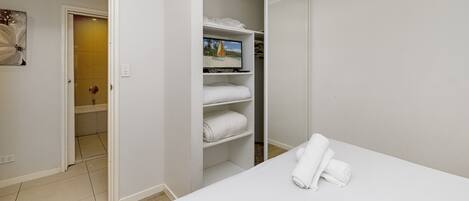 A hotel room with a bed, a closet with shelves, and a door leading to a bathroom.