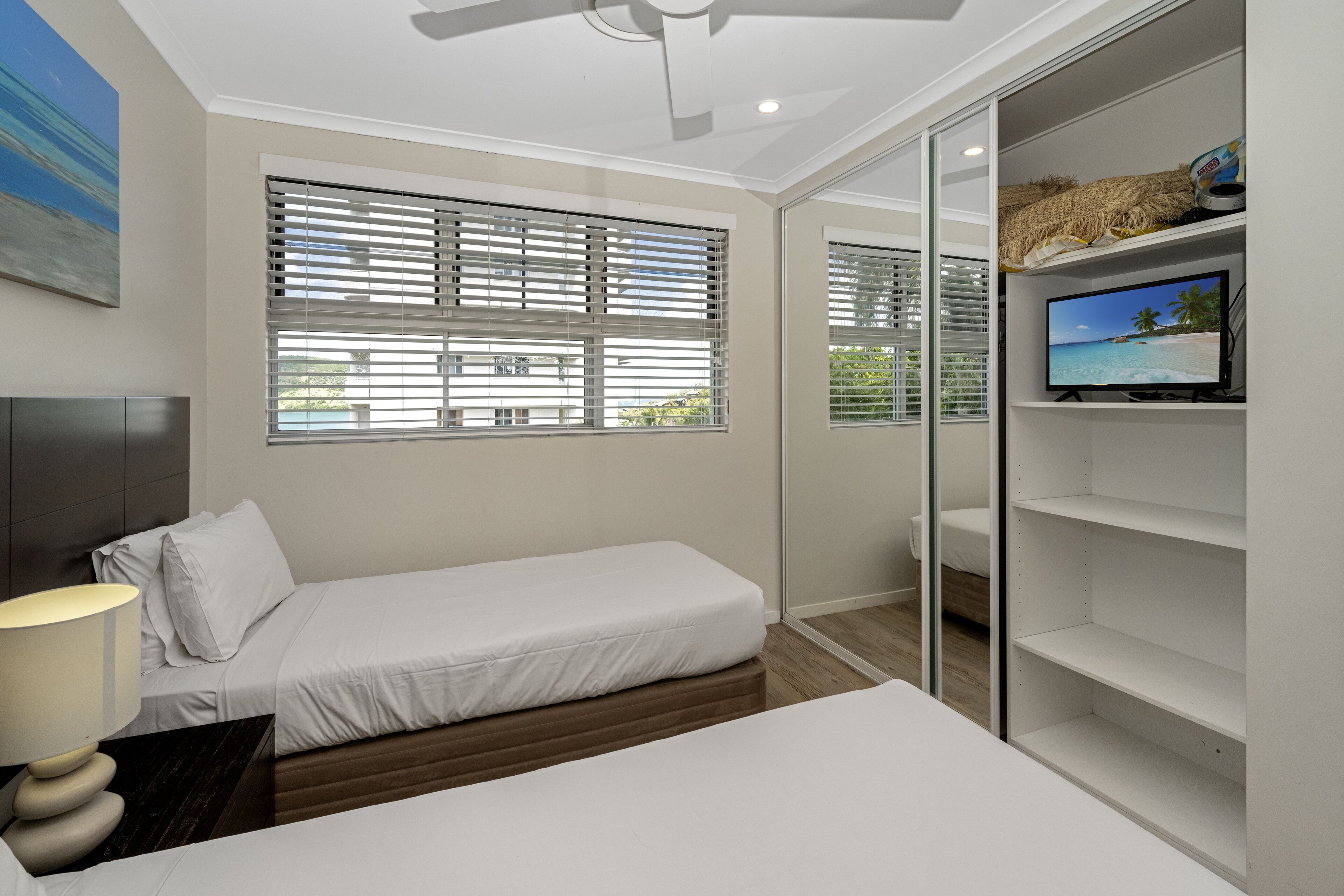 A modern bedroom with a single bed, a TV on a shelf, and a ceiling fan.