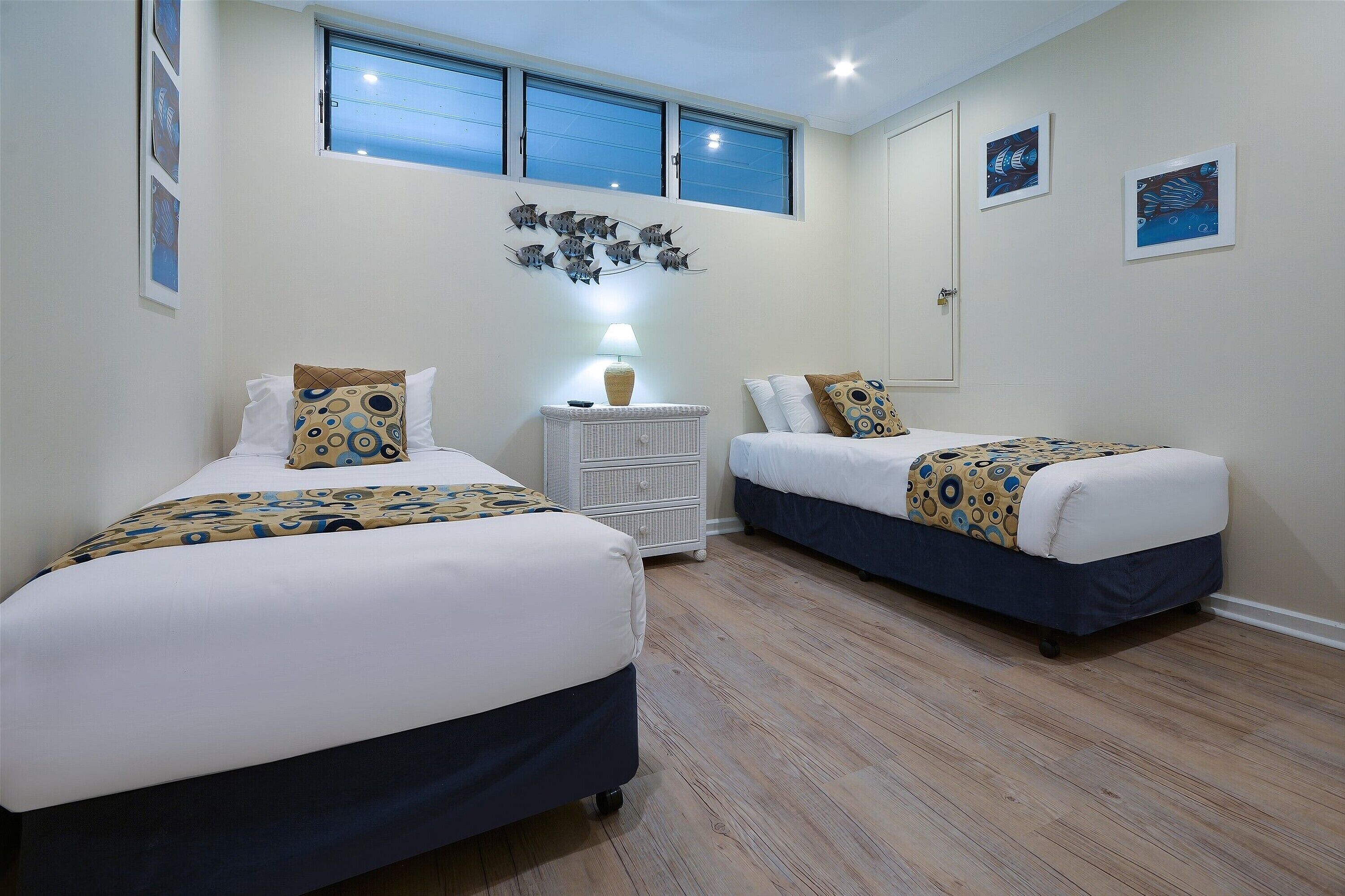 Un dormitorio con dos camas, una mesita de noche y una decoración de peces colgada en la pared.