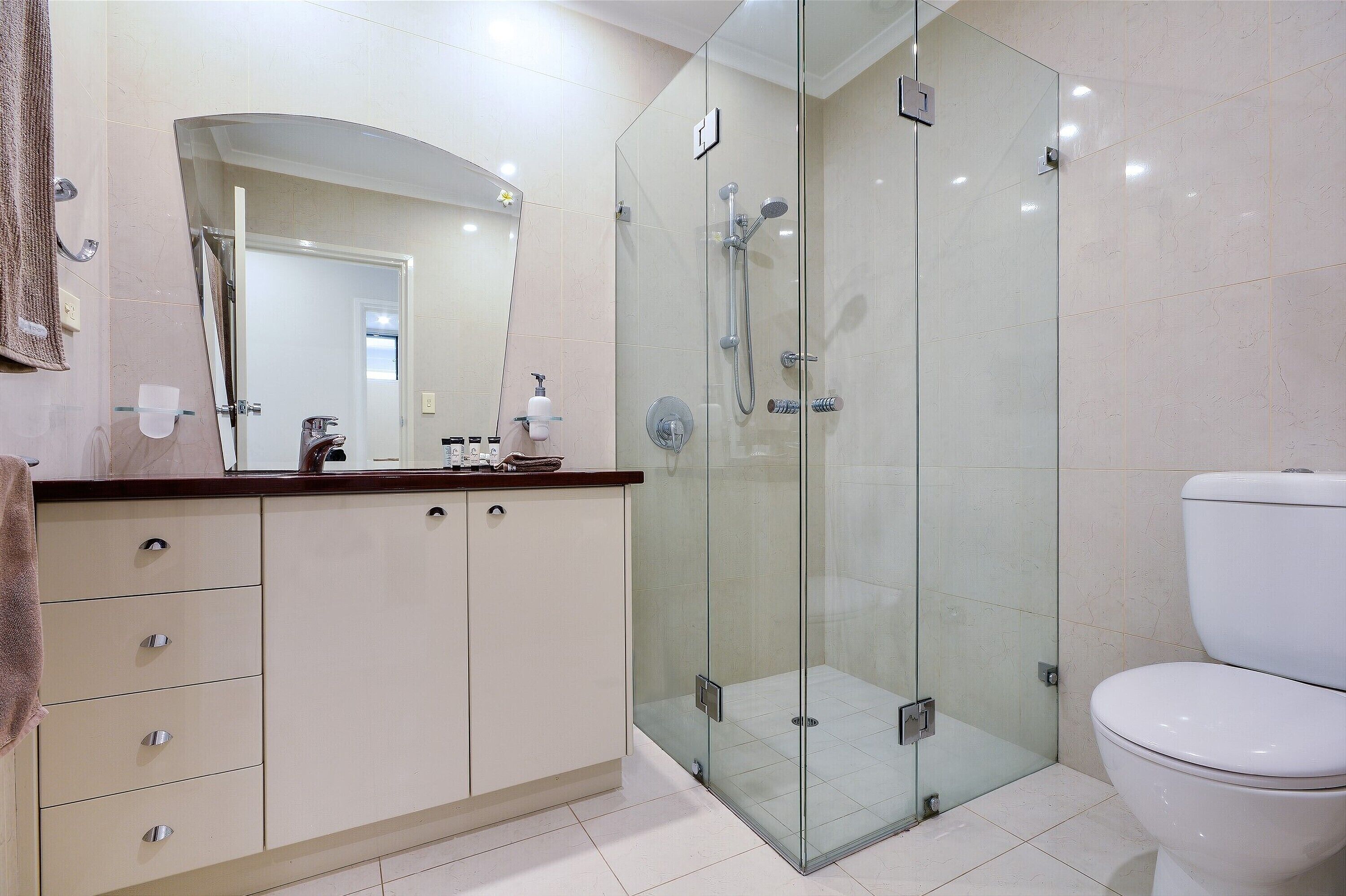 Un baño moderno con ducha de vidrio, inodoro blanco y tocador con cajones.