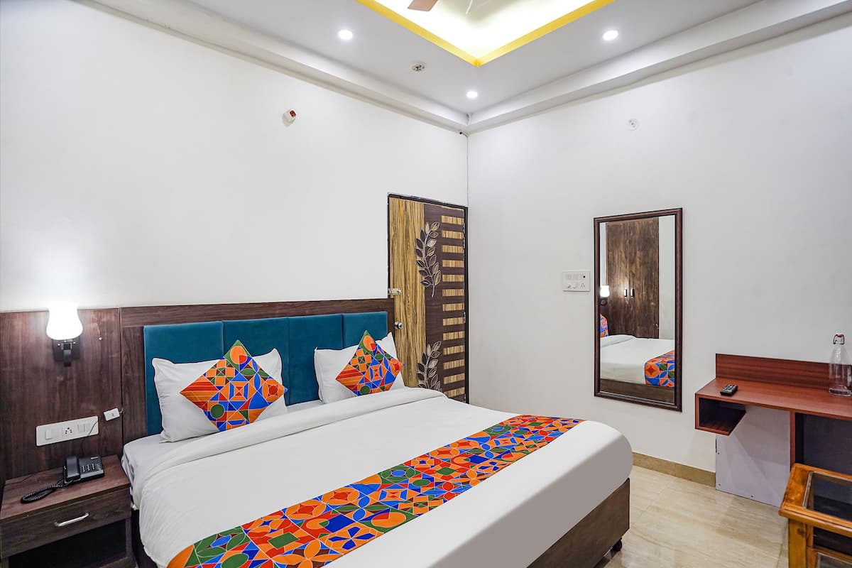 A hotel room with a bed, bedside table, nightstand, and a mirror.