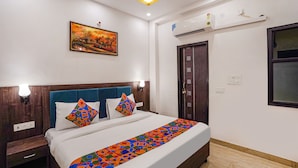 Una habitación de hotel con una cama, una mesita de noche, un aire acondicionado de pared, una puerta y una ventana.