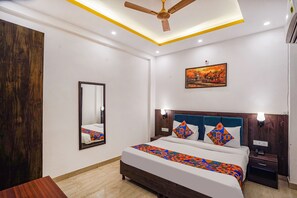 Habitación de hotel con cama, mesita de noche, espejo, ventilador de techo y un cuadro en la pared.