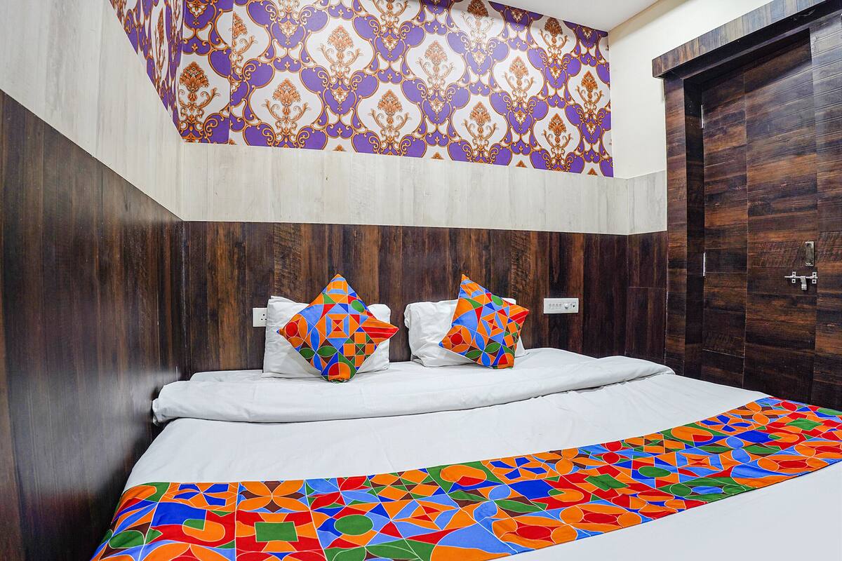 Een hotelkamer met een houten hoofdeinde, een gestreept plafond en een groot bed met kleurrijk beddengoed.