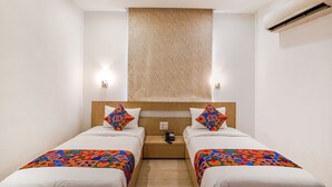 Een hotelkamer met twee enkele bedden, een houten hoofdbord, een klein nachtkastje met een telefoon en een airconditioner aan de muur.