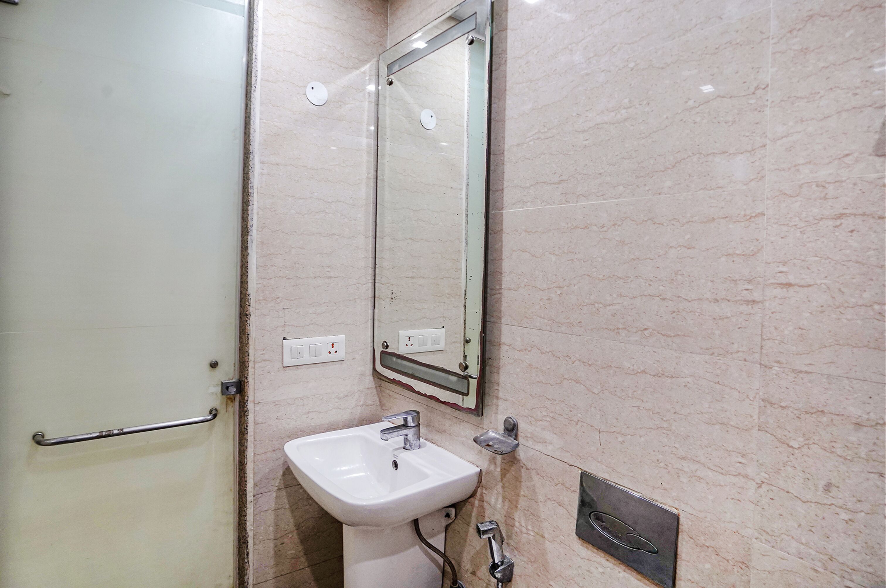 A bathroom with a white sink, a mirror, and a door with a handrail.