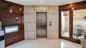 Een lift in een hal met marmeren wanden, een bankje en een bord waarop een kantoor wordt aangegeven.