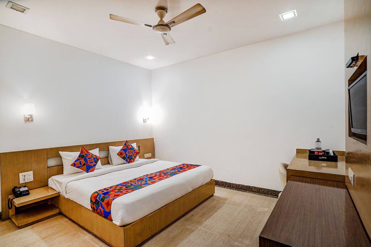 Een hotelkamer met een bed, nachtkastje, bureau en plafondventilator.