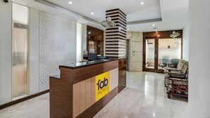 Een receptiebalie met een 'fab hotels' bord, een modern interieur met een behang met patroon, en een zithoek met gestreepte banken.