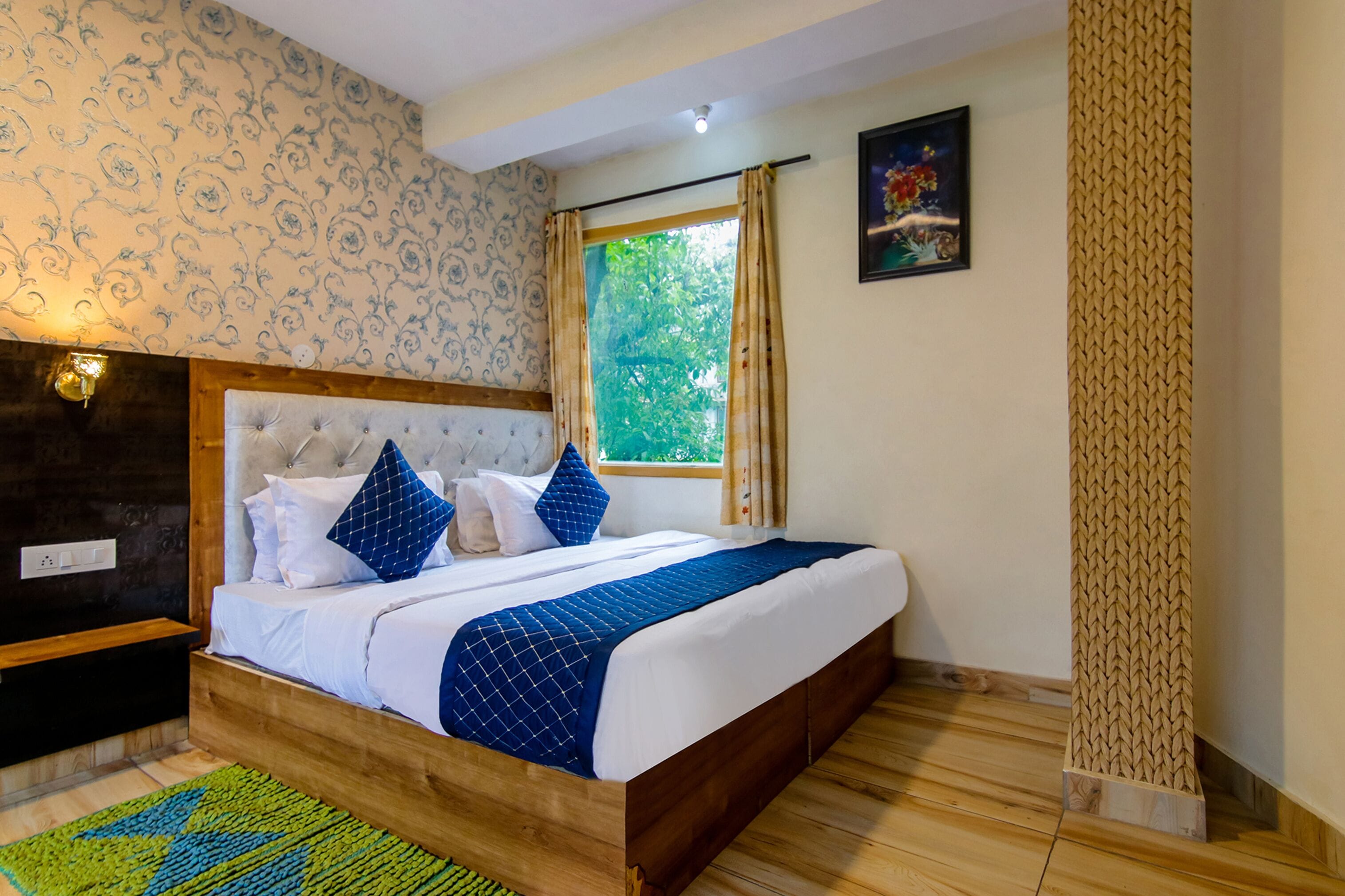 A bedroom with a wooden bed frame, a tufted headboard, and a view of greenery through a window with curtains.