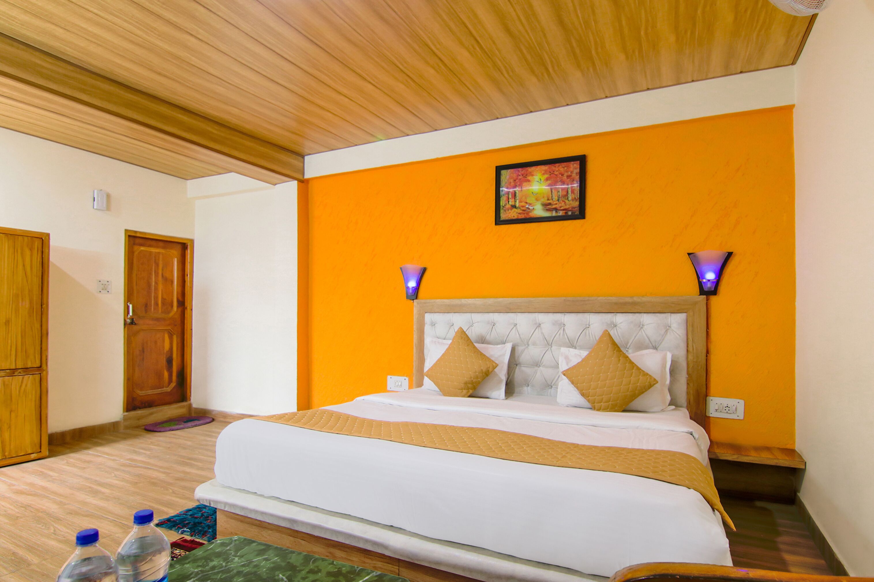 A hotel room with a bed, wooden ceiling, and orange walls.