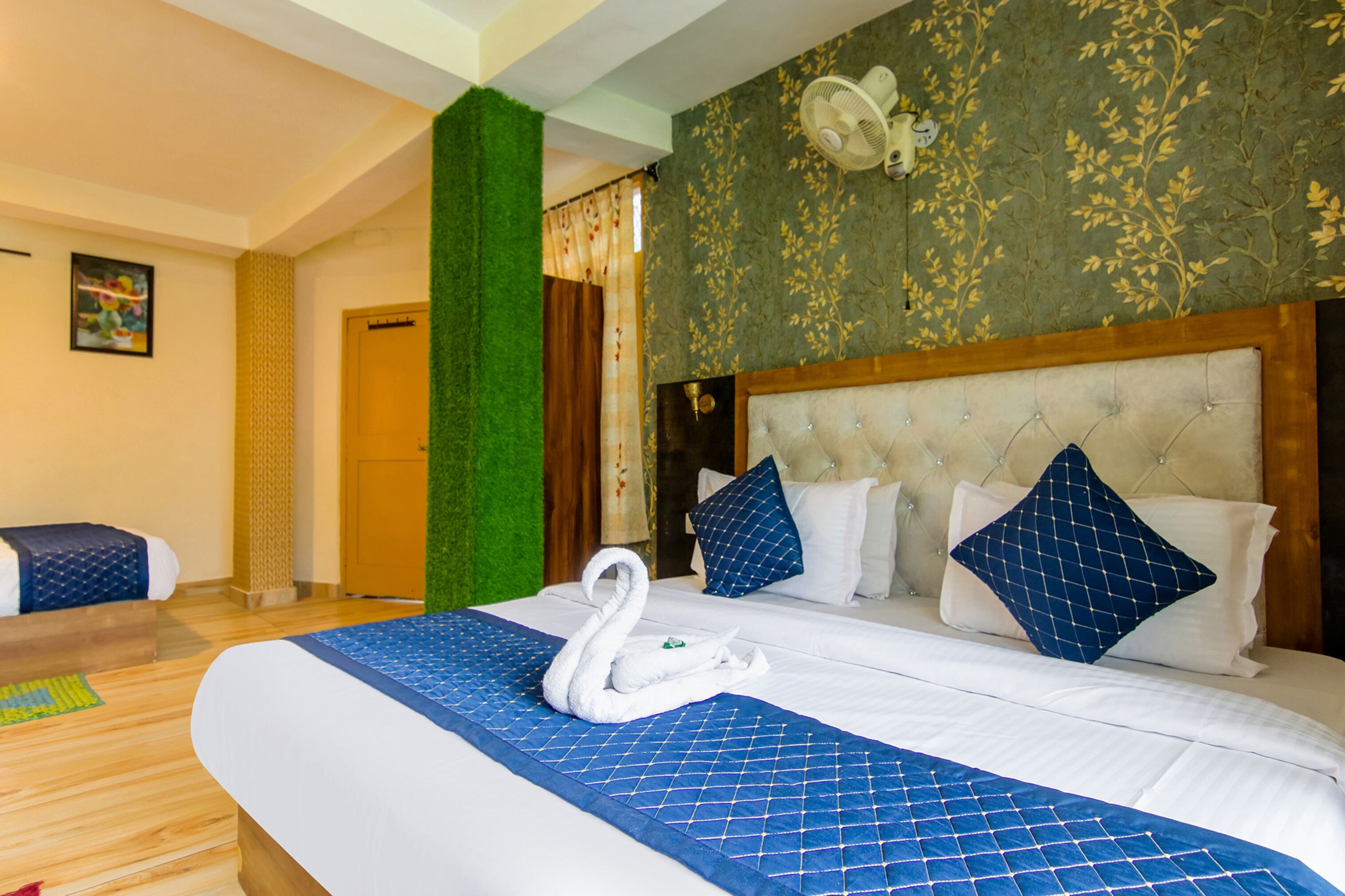 Ein Hotelzimmer mit einem großen Bett, einem gepolsterten Kopfteil und einem Wandventilator.