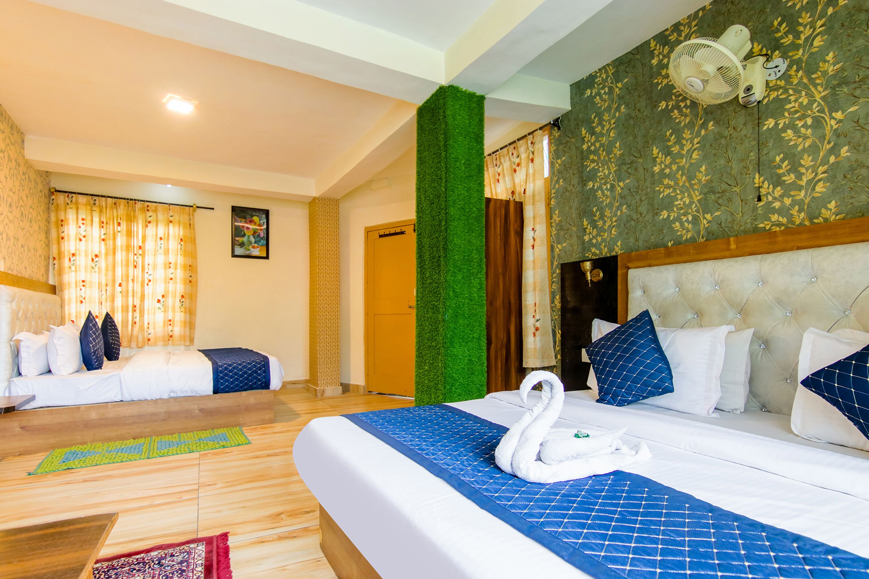 A hotel room with a large bed, a separate sofa, a green accent wall, and a ceiling fan.