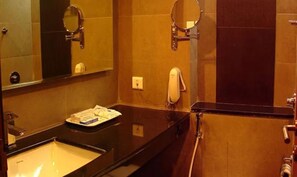 Baño de hotel con un lavamanos negro, dos espejos, un dispensador de toallas y un inodoro.